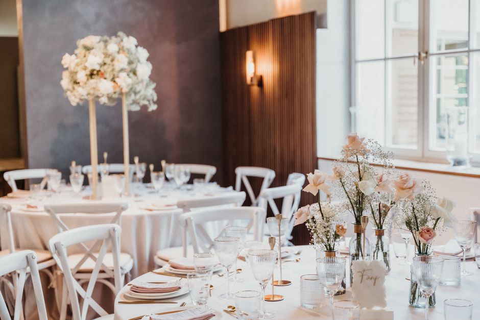 A floral arrangement featuring soft pink roses and white baby's breath in small clear glass vases, arranged on a white tablecloth at a wedding venue on Whetstone High Road N20. The flowers appear fres